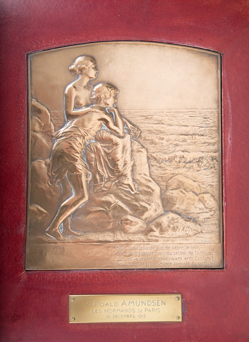 Relieffet viser en ung mann og en ung kvinne, begge iført et tyndt klæde rundt livet. De sitter på en stein og ser ut over havet.