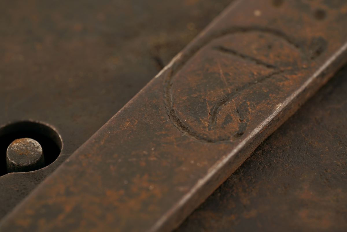 Hengelås av jern med svingbart lokk over nøkkelhull. Ova eller rund.
Nøkkel av jern. Gjennombrudt, hul, med forhøyning i nøkkelens overkant.