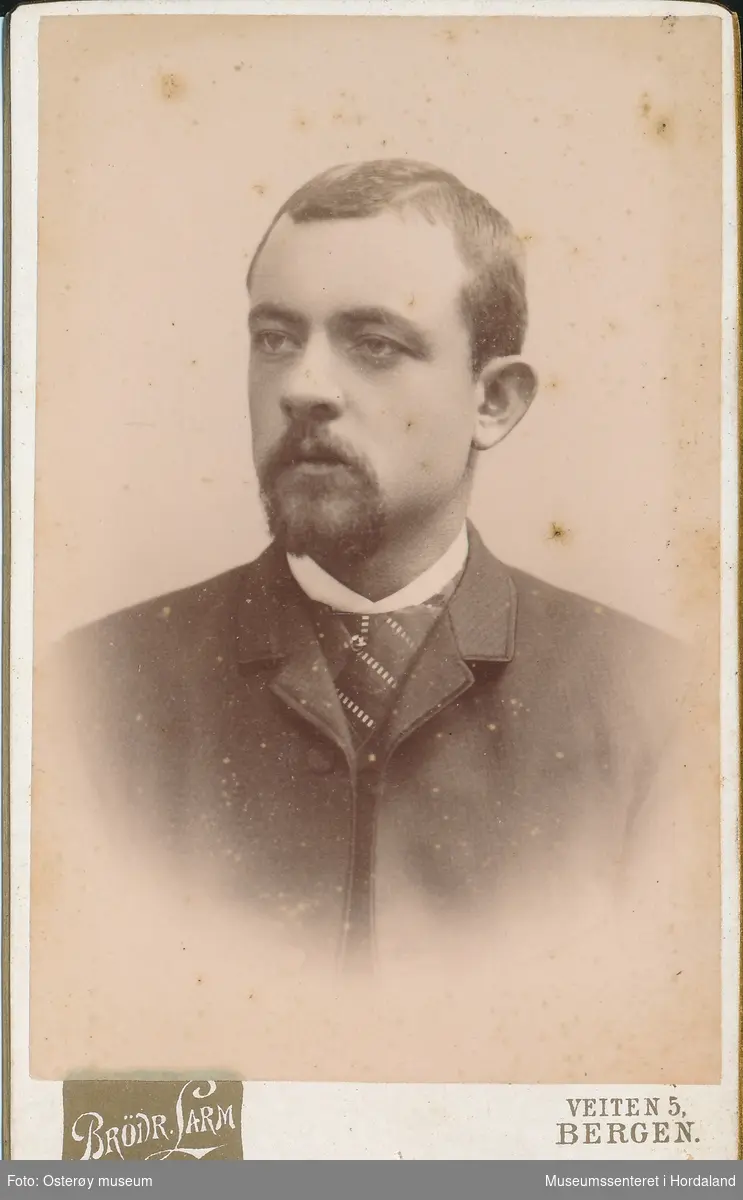 portrettfotografi av yngre mann med skjegg, mørk jakke, kvit  snipp og sjal
