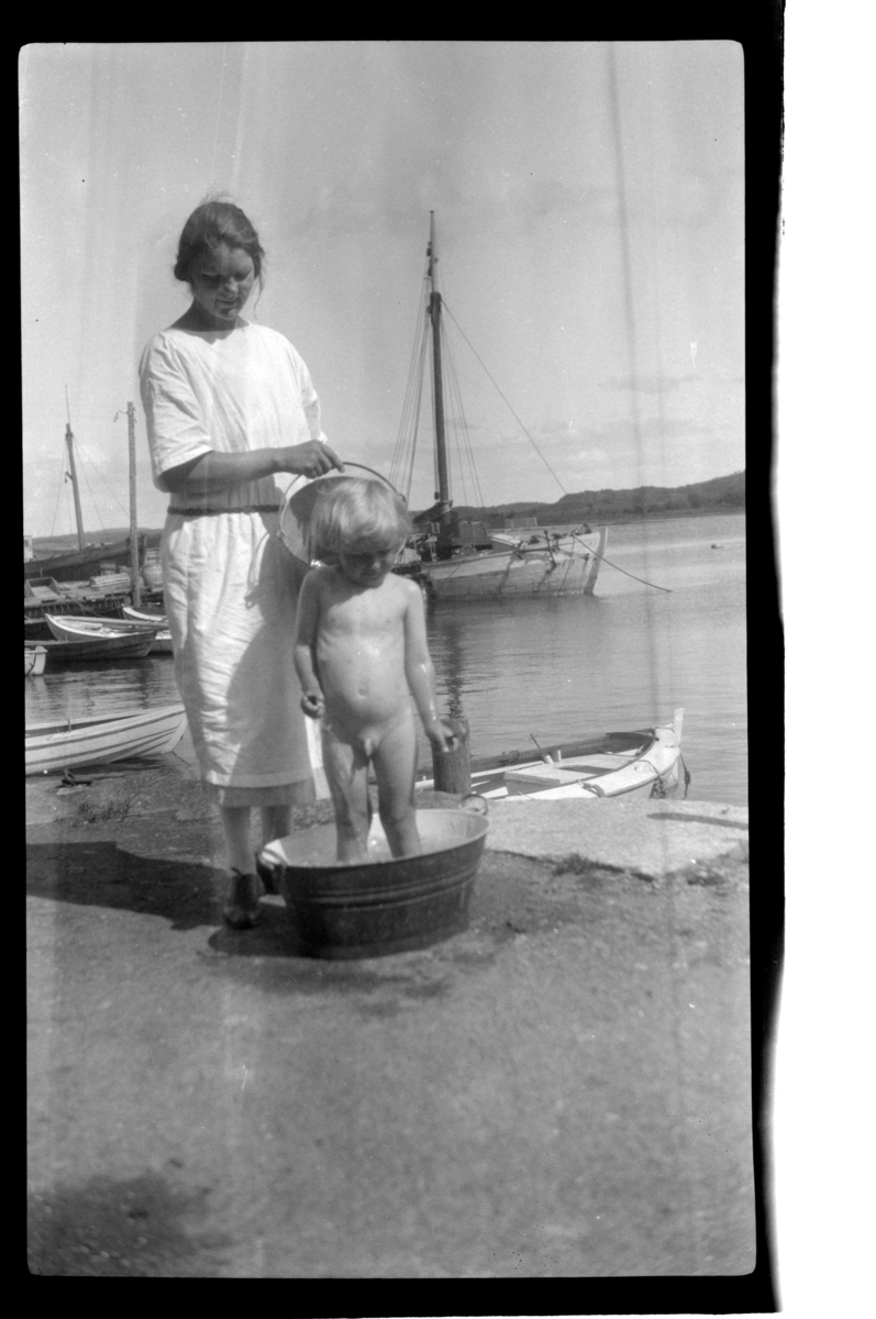Rolf Sundt Jr. vaskes i sinkbalje av ukjent kvinne ved båthavn i Slagen ved Tønsberg. Fotografert 1925.
