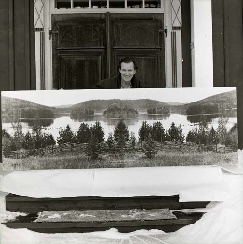 Hilding står på en förstukvist och håller upp en stor uppmonterad fotokopia. En panoramabild gjord genom att spegelvända motivet, december 1973.