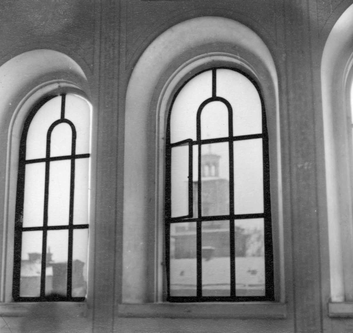 Perspektiv i nordvästlig riktning med vy mot Olaikyrkans klocktorn. Fotografiet taget från översta trapphusfönstret i kvarteret Korpen 19 som låg vid korsningen av Drottninggatan och Repslagaregatan i Norrköping 1953.