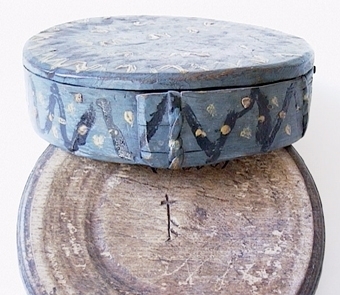 Rund träask med trycklock som målats i blått och ornerats med sicksacklinjer och punkter i vitt och svart.