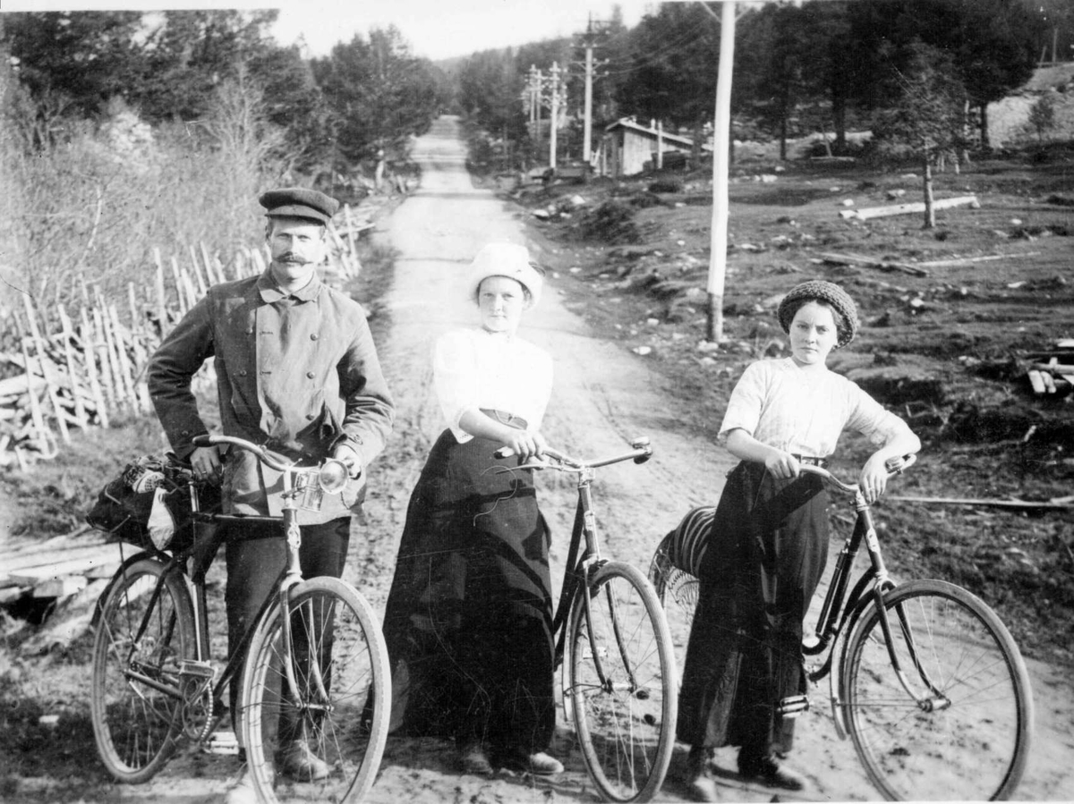 Repro: Syklister. To kvinner og en mann stående på en vei.