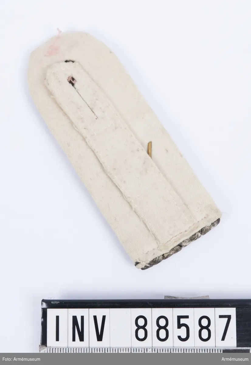 En axelklaff med fyra vävda snören av silvertråd med svarta inslag (preussens färger) och nummer "34" i mässing. Kantningen är av vitt kläde. Axelklaffen användes till den fredstida uniformen.