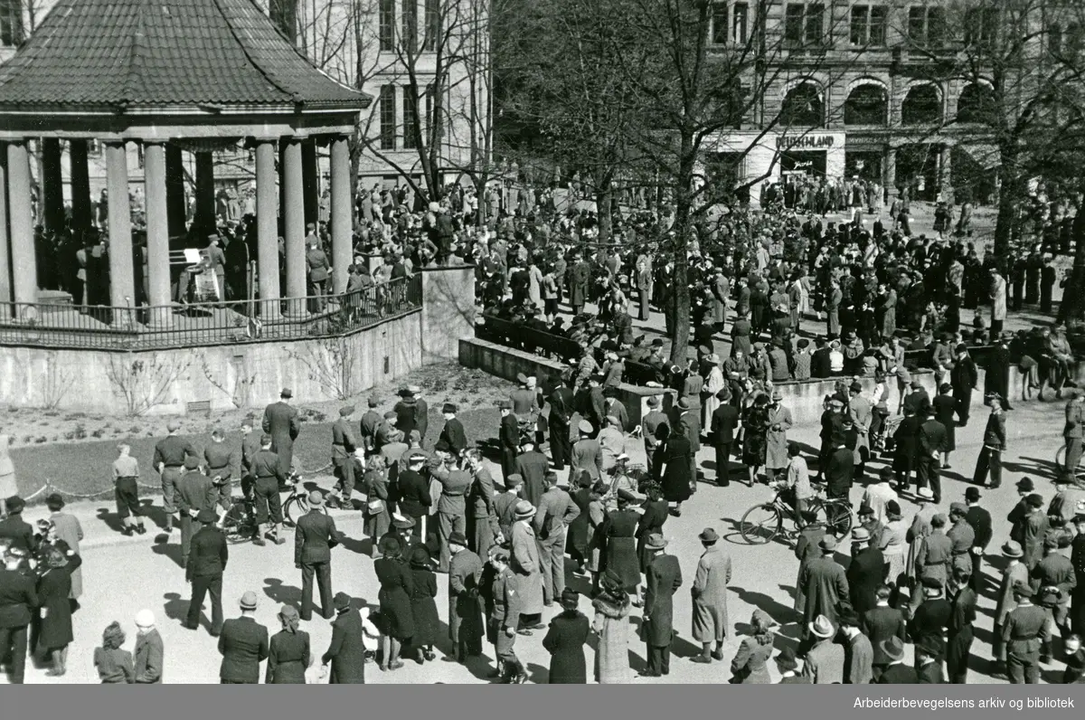 Antakelig et militærorkester eller den norske arbeidstjenestens musikkorps som underholder fra musikkpaviliongen på Karl Johans gate, mai 1943.