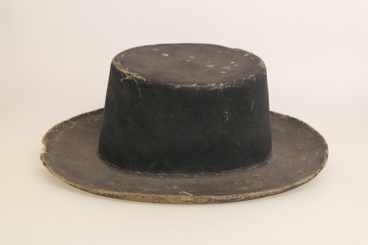 Svart filthatt med stiv pull og brem. Pullen er flat på toppen. Hatten er muligens malt svart.