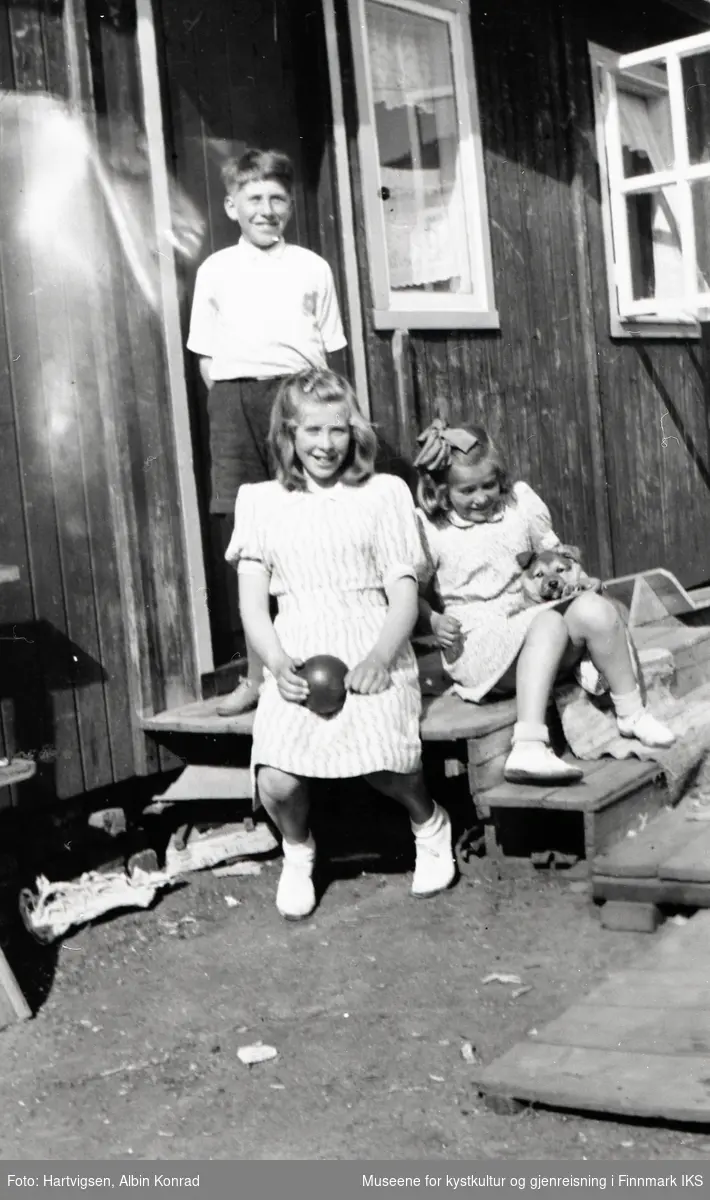 Honningsvåg. Gjenreisning. Søskene Ann (t.v.), Aud og Rolf Jensen på brakketrappa. Aud Jensen holder en liten hund. Sommer 1947.