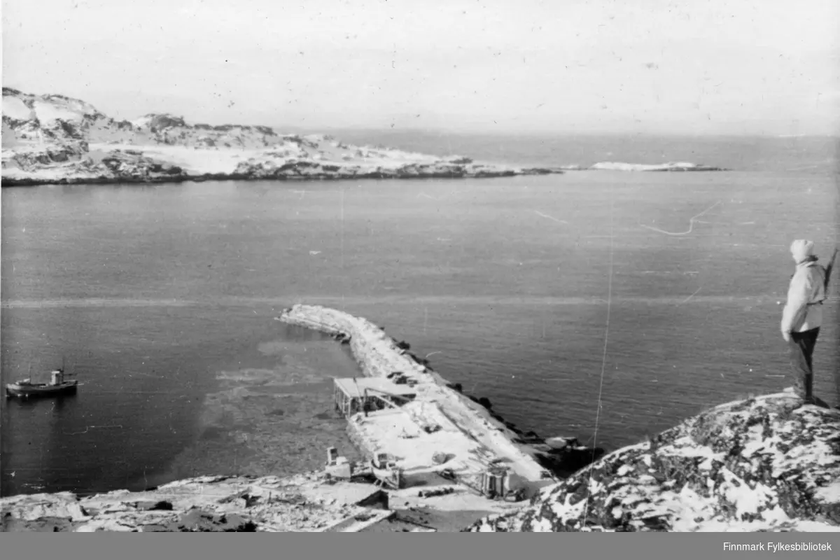 En soldat fra 2.Bergkompani står vakt på en høyde over snedekket landskap, han har skaller på bena.  Stedet er Holmefjord, Porsanger, 1944/45. I bakgrunnen ser man en branntomt, en lang molo og en fiskebåt. Et par fiskebåter ligger på land. Det kan være m/k "Glimt" av Sørøya som ligger for anker. F64HV - 29fot lang. Før den ble tatt i Sortvik under den såkalte "Tragedien i Sortvik". Båten var i tjeneste under Rognstad og Bergkompaniet og stasjonert i Holmenfjord. Skipper og eier var Johan Eilertsen. Både Johan Eilertsen og Ragnar Jensen mistet livet 21.02.1945, begge fra Breivikbotn. 


Bildeserien "Frigjøringen av Finnmark 1944-45" viser et unikt materiale fotografert av soldater i Den Norske Brigade, 2. Bergkompani under deres oppdrag "Frigjøringen av Finnmark" som kom i stand under dekknavn "Øvelse Crofter". Fakta rundt dette bildematerialet illustrerer iflg. vår informant, George Bratli: "2.Bergkompani, tilhørende Den Norske Brigade i Skottland,  reiste fra Skottland 30. oktober 1944 med krysseren «Berwick» til Scapa Flow på Orkenøyene for å slutte seg til en større konvoi som skulle være med til Norge. Om bord på andre skip var det mange russiske krigsfanger som hadde vært på tysk side og som nå ble sendt hjem. 
2.Bergkompani forlot havn 1.november 1944 og kom til Murmansk, Sovjetunionen, 6. november 1944. 
De ble her lastet om og fraktet til Petsamo, Sovjetunionen, hvor de ankommer 11.november 1944. 
Kompaniet reiser så til Sandnes utenfor Kirkenes og blir forlagt der frem til 26.november 1944. De flytter så videre til Skipparggura. 
Den 29.november reiser deler an kompaniet til Rustefielbma og Smalfjord og noen drar opp på Ifjordfjellet. 

17. desember ankommer resten av kompaniet til Smalfjord. 30.desember blir en avdeling sendt til Hopseide og 8. januar 1945 blir noen sendt til Kunes.
Den 14. januar er kompaniet delt og ligger i Kunes, Kjæs, Børselv, Hopseide og Smalfjord.
5. februar 1945 blir 3.tropp sendt over Porsangerfjorden for å operere i Olderfjorden. Her var de i kamp og hadde tap i  Billefjord og Sortvik.
8.mars 1945 kom noen til Renøy og 12. mars kom første del av kompaniet til Brennelv.
7.mai begynte kompaniet å bygge ny kai i Hambukt.
19. mai ble de som hadde falt begravd i Lakselv.
8. juni ble kompaniet flyttet fra Brennelv til Tromsø for så å bli sendt videre til Mo I Rana 16.juni."

Nasjonalbiblioteket har et hefte fra 1983 skrevet av Krigsinvalideforbundet, med intervjuer med soldater og deres opplevelser: 
https://www.nb.no/items/5d58d366b390666f671f57078519c2c7?page=0&searchText=Det%20glemte%20kompani%20-%202.%20Bergkompani%20og%20frigj%C3%B8ringen%20av%20Finnmark

https://www.arkivverket.no/utforsk-arkivene/andre-verdenskrig/befolkede-jordhuler-kjokken-i-det-fri-og-midlertidige-begravelser-privat-bildesamling-etter-soldat-i-2.bergkompani
