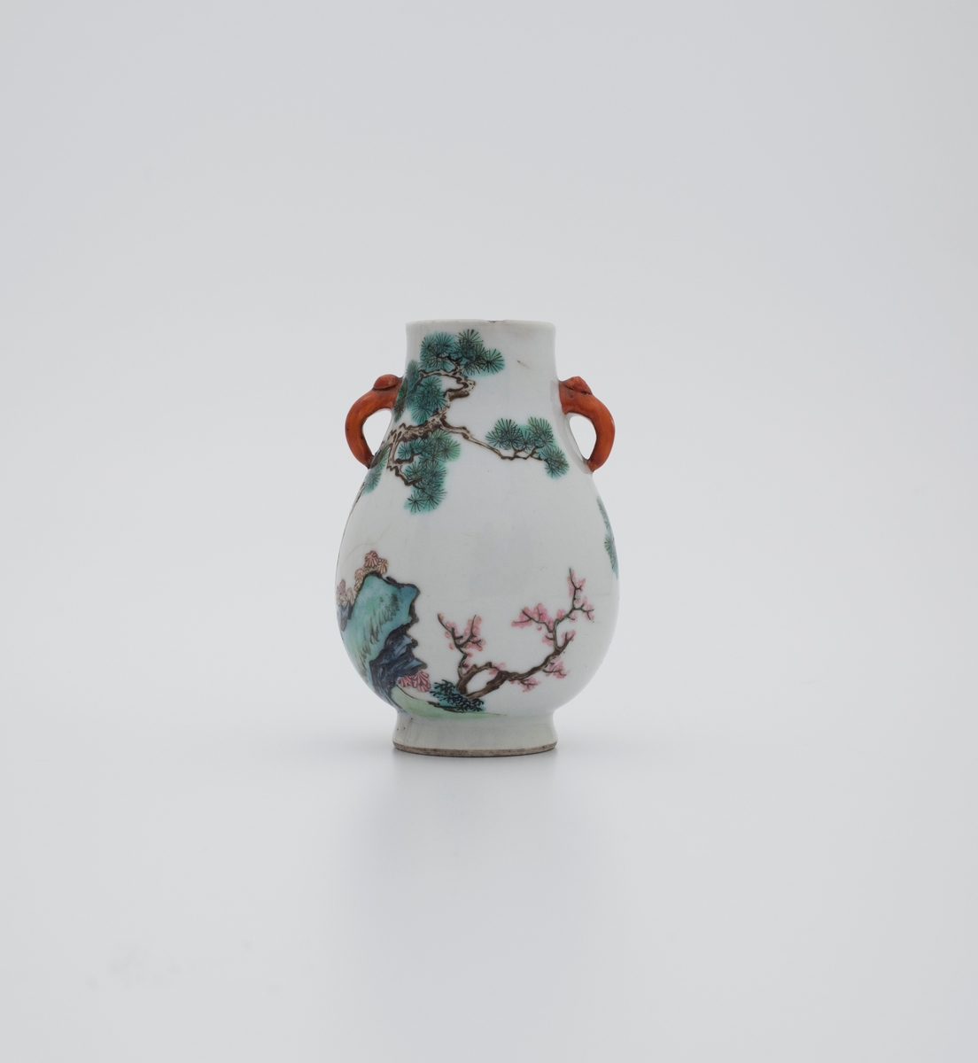 Famille rose vase med kirsebærblomst, furutrær, stein og traner. Tranen fremstilles ofte i kombinasjon med furu og stein, og er som oftest brukt som et symbol for langt liv. Håndtakene er utformet som elefanthoder.