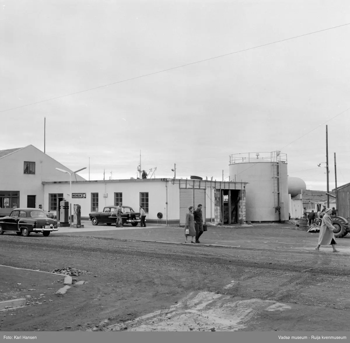 Vadsø sentrum 1959. Bildet tatt fra krysset Tollbugata/W.Andersens gt. Shells bensinstasjon i Tollbugata og tankanlegg for drivstoff/brenselsolje. Vi ser bensinpumper. En mann arbeider på taket.