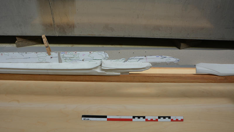Nærbilde av 3D-printede kjøldeler i hvit plast montert på treramme. Et av kjølbordene i papp er også montert på babord side av kjølen.