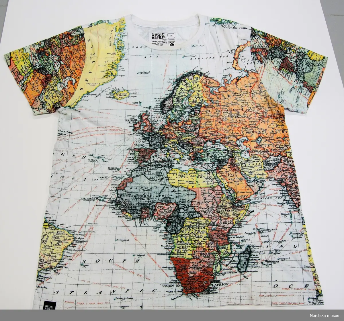 T-shirt av 100% bomull. Kort ärm, rund halslinning. Raka stycken, Tryckt mönster i form av färgrik karta (Europa, ryssland och Afrika). Samma tryck på både fram- och baksida. 
Etikett på insidan av bakstycket (nacken) med text "DEDICATED M [M=storleksangivelse] / 100 ORGANIC AND FAIRTRADE CETIFIED COTTON / DESIGNED AND PRINTED IN SWEDEN MADE IN INDIA / DO NOT IRON ON PRINT / TURN INSIDE OUT WHEN WHASING / WWW.TSHIRTSTOREONLINE.COM" samt tvättsymboler för 30 grader, ej klorblekning, torktumling på låg temperatur, strykning (ej angivet några prickar), ej kemtvätt.
Liten svart etikett i nederkant på höger sida av framstycket "DEDICATED". 
/Leif Wallin 2017-07-13