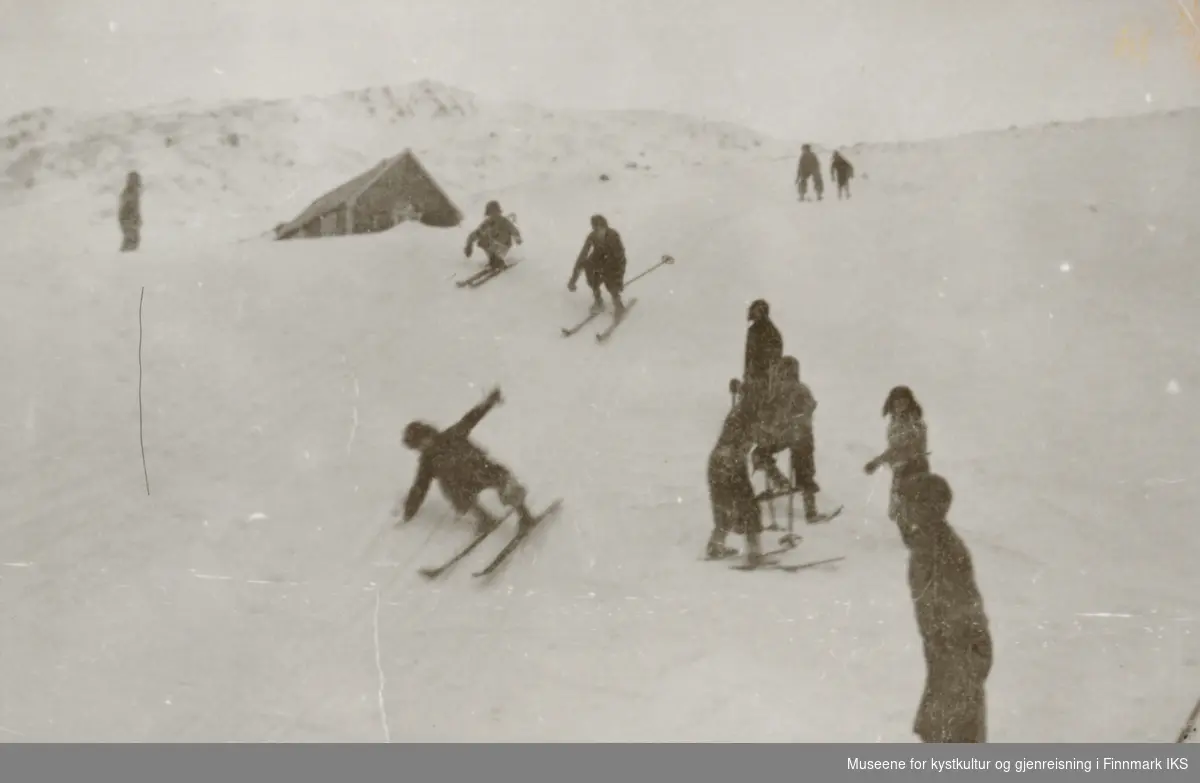 Honningsvåg. Barn på ski nedover en bakke i Elvedalen. I bakgrunnen Eyvind Larsens bolighus. 1930-tallet.