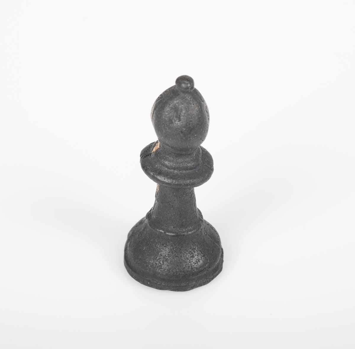 Sjakkbrikken (løper) er laget av tre, og er malt svart. Et lite område uten maling. Et lite avlangt hull på undersiden.