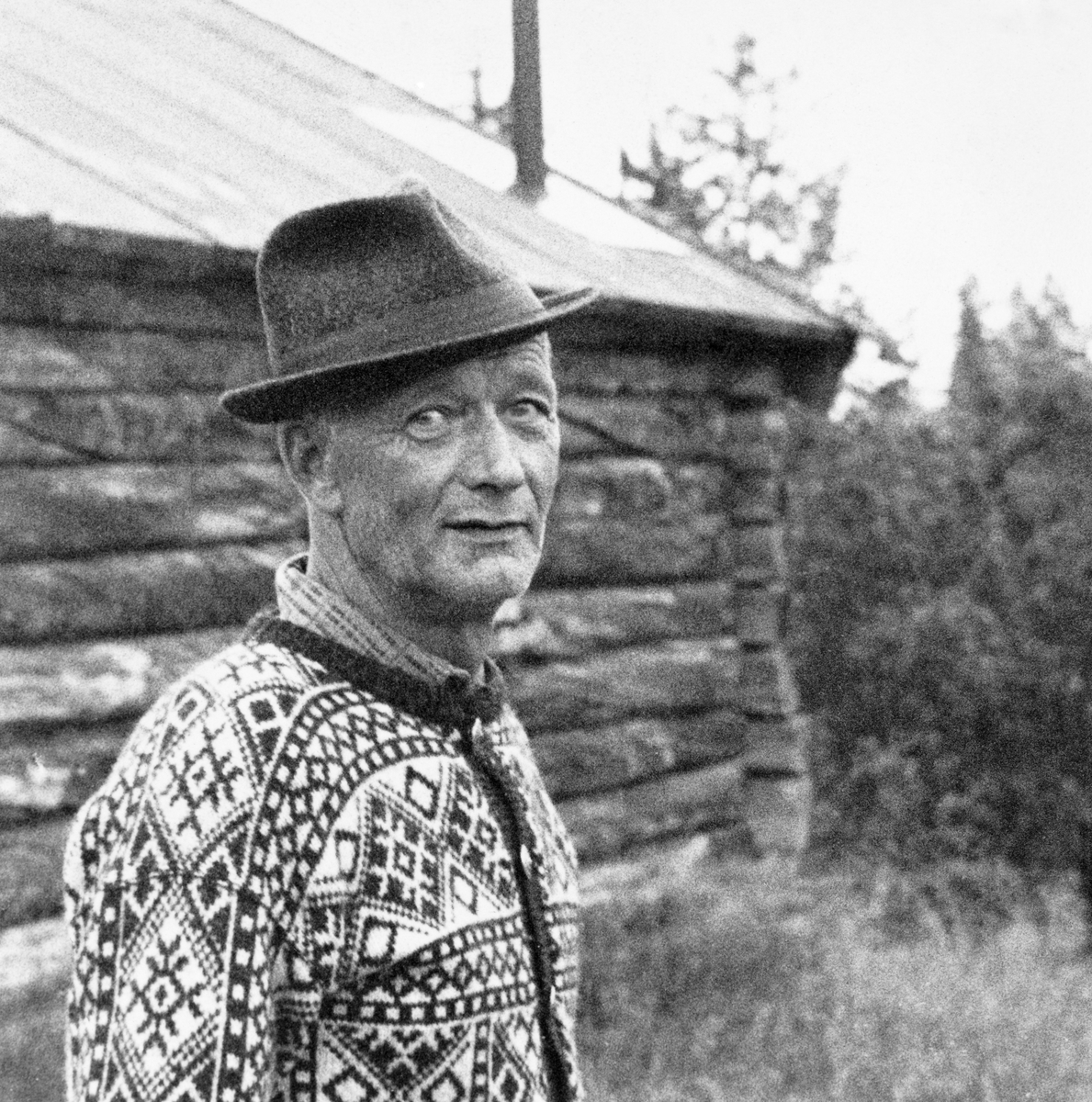 Tømmerkjører Bernhard Bordi (1909-1995) i Pasvikdalen.  Bordi er fotografert i strikkejakke og med hatt foran ei koie.  Fotografiet er brukt i en artikkel om Bordi i tidsskriftet Statsskog nr. 2 1976.