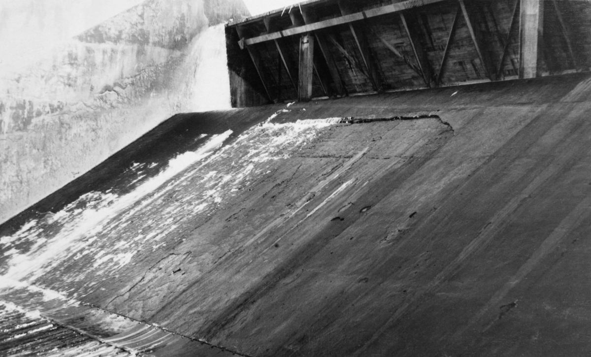 Detalj fra tømmerløpet i kraftverksdammen som ble bygd ved Osfallet i elva Søndre Osa i Åmot kommune i Hedmark.  Fotografiet er tatt i september 1915, et snaut år etter at kraftverket ble satt i drift.  På opptakstidspunktet var det åpenbart liten vanngjennomstrømming i elva, slik at en lett kunne se den glatte betongen som bare delvis var dekt av et tynt vannslør.

Osfallsdammen ble ødelagt under vårflommen i 1916, og dambruddet forårsaket store skader på det nye anlegget, noe som innebar betydelige økonomiske tap for utbyggerne, Åmot kommune.  Mer informasjon om kraftutbygginga ved Osfallet og det påfølgende dambruddet finnes under fanen "Opplysninger".