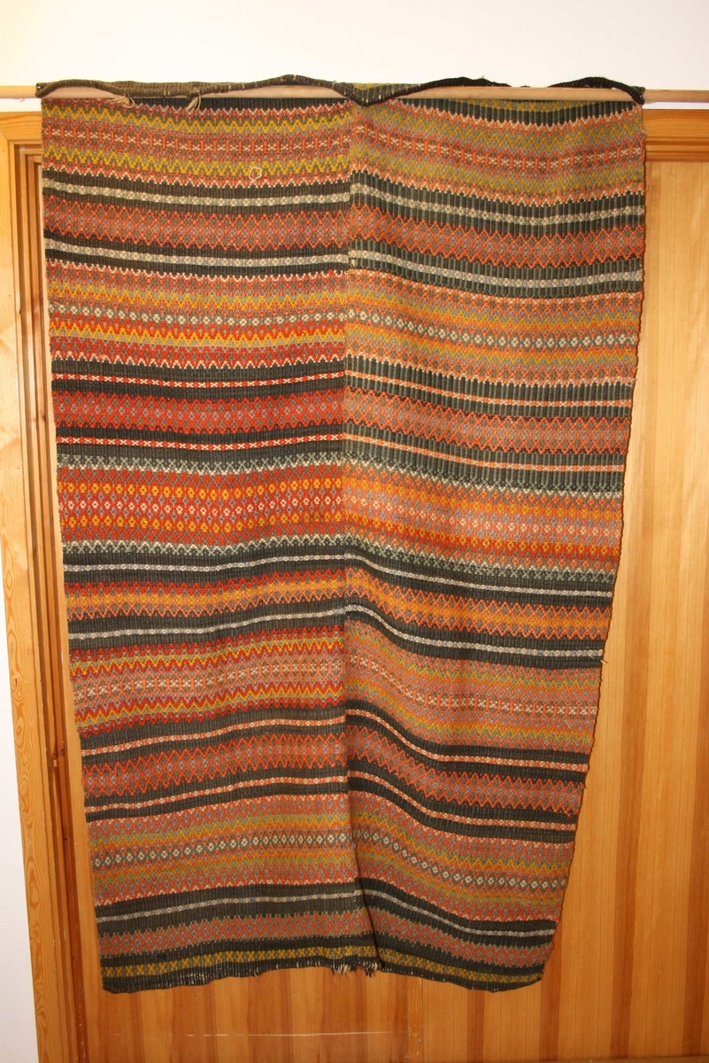 Rektangulært teppe med mønster, sydd saman av 2 breidder, falda  i båe endar.