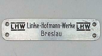 Långsmal rektangulär aluminiumskylt med rundade hörn. Svart text: "LHW Linke-Hofmann-Werke Breslau LHW". Tillverkarskylt från motorvagn nr 8, SNJ