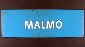 Rektangulär dubbelsidig plastskylt med vit text på blå botten: 
"HALMSTAD".

På andra sidan:
"MALMÖ".