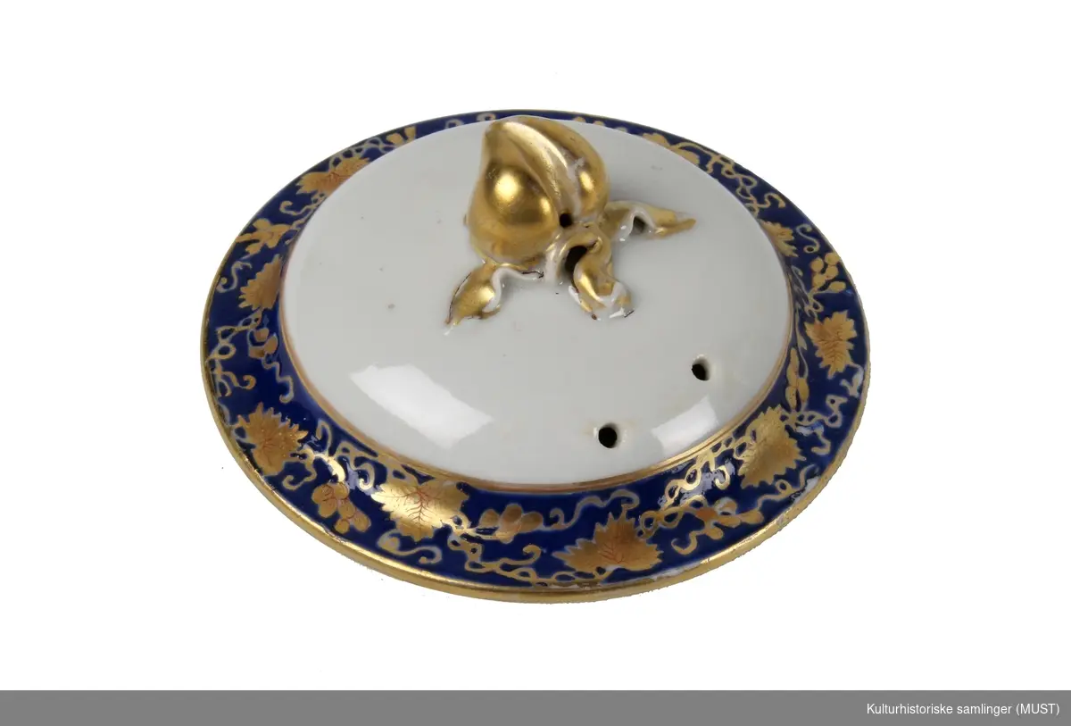 Sjokoladekanne, sylinderformet svungen hank og tut. Lokk m/lokkgrep. Langs kanten emaljeblå bord med vinløv i gull og rødt og på siden en oval innskrift.