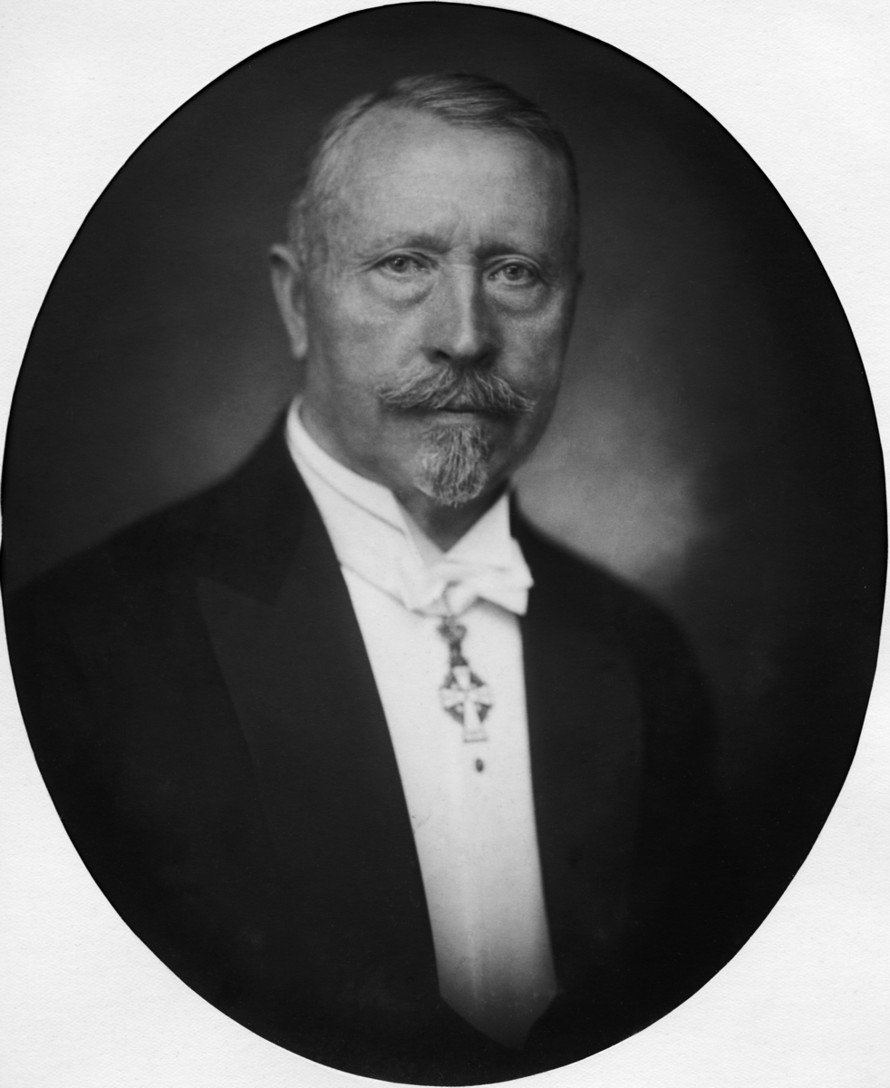 Portrettfotografi av trelasthandler og skipsreder Hans Halvorsen Holta (1859-1941) som var en høyt profilert forretningsmann i Skien og på Notodden.  Fotografiet er et studioopptak.  Holta var kledd i smoking.  Han hadde et kvitt, stivet skjortebryst med flippkrage, kvit sløyfe og et slags smykke - antakelig dannebrogsordenen - som hang i et kvitt bånd under sløyfa.  Dette smykket er formet som et kvitt (antakelig emaljert) kors på et sirkelformet underlag, muligens en stillisert krans.  Da dette fotografiet ble tatt var Holta en godt voksen mann, antakelig over 60 år.  Han hadde grått fippskjegg, grå bart og grått, kortklipt og sidekjemmet hår med høyt hårfeste.  Han er portrettert med et fast blikk vendt mot fotografen og betrakteren av fotografiet.  Fotografen har gjort ansiktet skarpt, mens det øvrige er noe sløret.  Bildet er montert i oval papirpassepar-tout. 

Dette portrettet av H. H. Holta er innkommet fra Skiensvassdragets Fellesfløtningsforening.  Han kom i kontakt med denne virksomheten etter at han begynte å arbeide for sin bror, Ole Havlvorsen Holta i selskapet Blakstad, Holta & Co.  Broren var styreleder for virksomheten fra slutten av 1890-åra til 1910.  Ole Halvorsen Holtas siste år som styreleder var preget av mistillit fra de andre tømmerkjøperne etter at han som leder for Tinfos Papirfabrik hadde initiert inngrep i Tinnfossen som skapte problemer for fløtinga.  I mellomtida møtte Hans H. Holta i Fellesfløtningsforeningens generalforsamlinger som representant for Telegrafpælekompaniet.  Hans ble valgt inn i fløtingsstyret det året broren Ole trakk seg, og han var styreleder for virksomheten fra 1917 til et årsmøte som ble holdt på nyåret i 1928.  Dette innebar var øverste tillitsvalgte i Skienavassdragets Fellesfløtningsforening i en vanskelig periode som omfattet både «tømmerkrakket» i 1921 samt den økonomiske depresjonen og de store streikene i åra som fulgte.