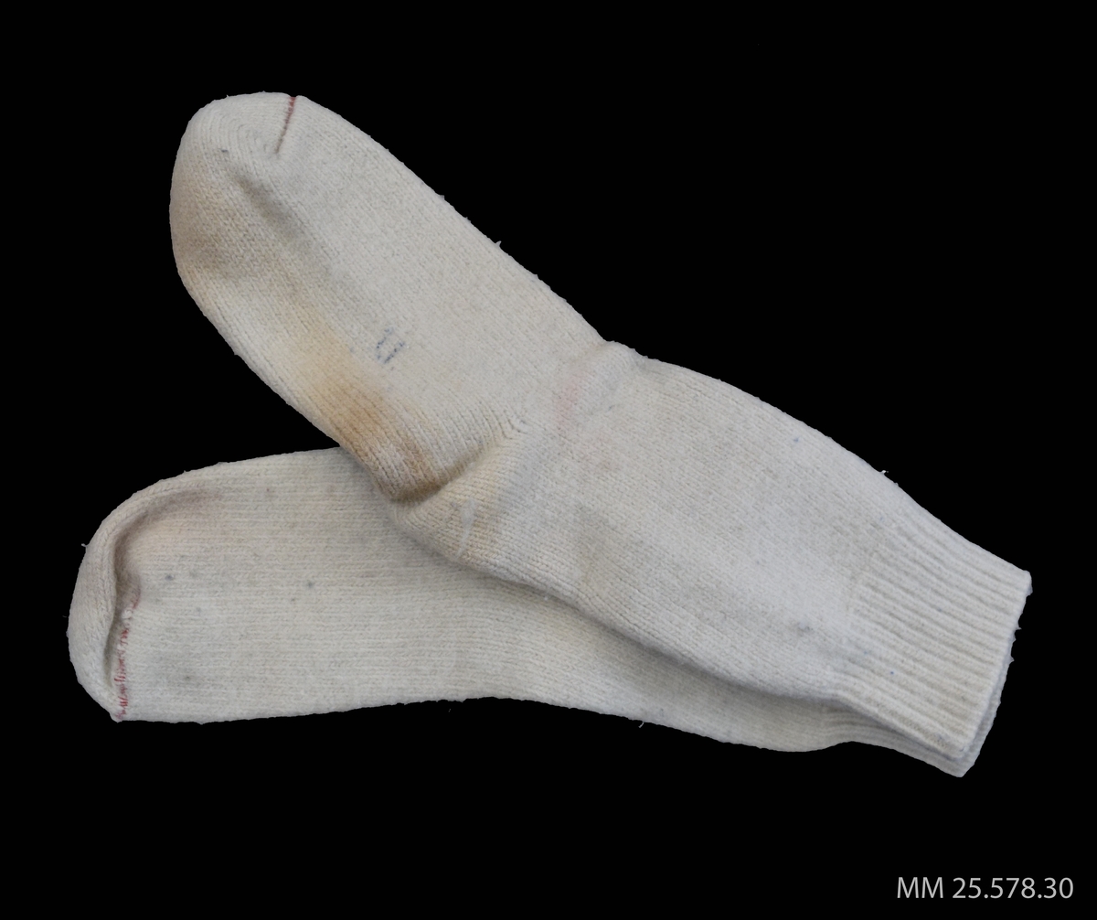 Vita strumpor eller sockor i ylle. Att bäras som förstärkning utanpå de "vanliga" strumporna. 
Vid tån på varje strumpa en röd rand som anger storlek.