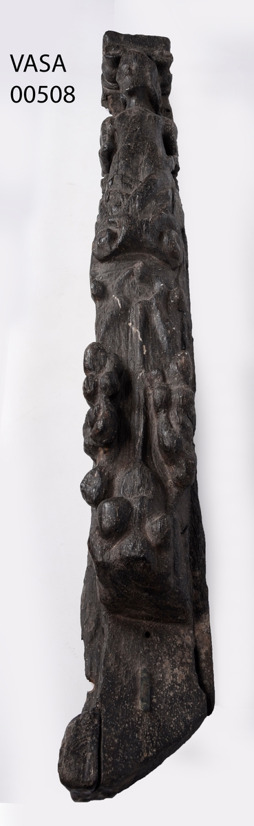 Pilaster föreställande en naken herm under joniskt kapitäl.
Hermen är iförd en stor hjälm. Huvudet är vridet åt höger.
Nedtill är pilastern prydd med en stor rullverksvolut och fruktornament. Fotändan har formen av en tunn, snedskuren och slät tapp eller tunga, med en något kilformad profil, som kan beskrivas som en fortsättning på bakstycket. Skulpturens baksidan är slät.
Skulpturen är relativt välbevarad. Ansiktsdragen är dock utplånade och händerna är bortnötta.

Text in English: Sculpted pilaster with naked Herm, under an Ionic capital.
The Herm is probably wearing a large helmet. The head is turned to the right.
The lower part of the pilaster is decorated with a large scroll-work volute and fruit ornamentation. The foot end is shaped as a thin, smooth, angled tenon (rather wedge-shaped in profile) that may be described as an extension of the backboard. The rear side is smooth or flat.
The sculpture is rather well preserved, but the features of the face obliterated and the hands are worn away.