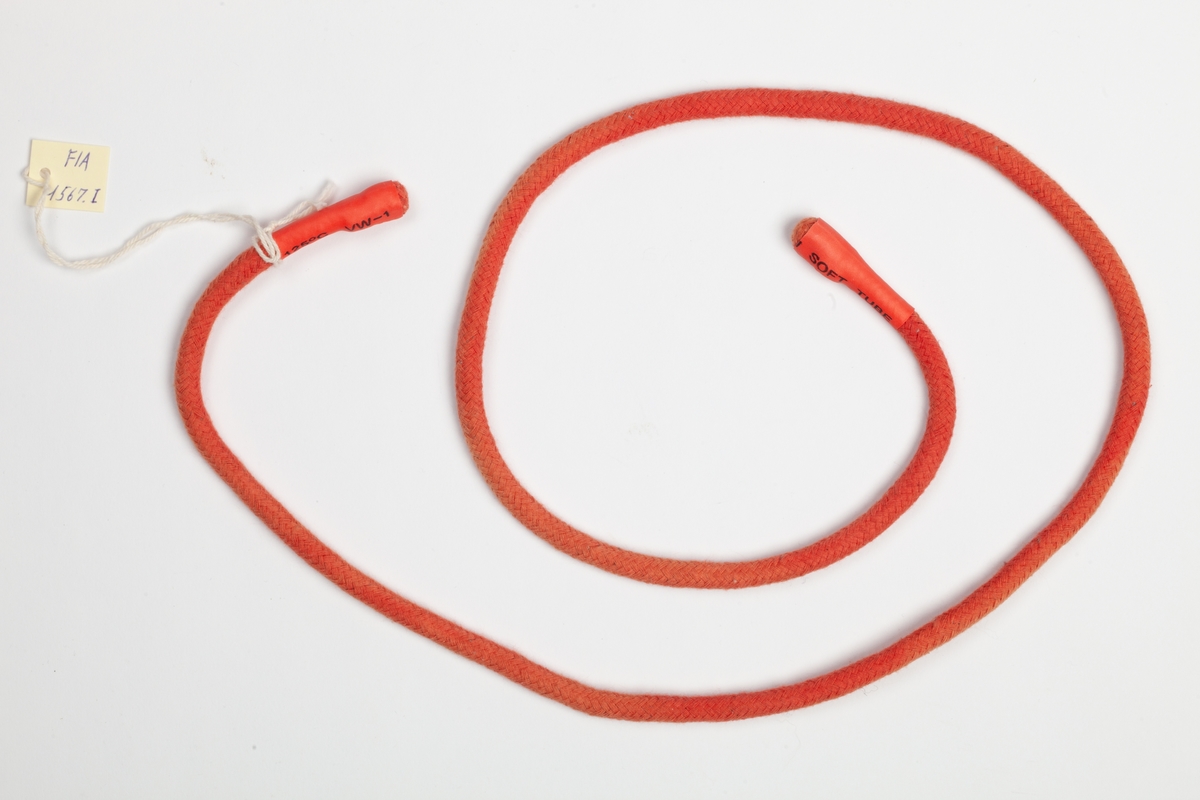 En rundvevet rød smal rem med gummiender. Turnikèen kan snøres sammen om et lem ved livstruende skade eller huggormbit.