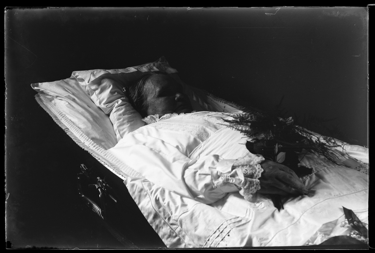 Tilda Pettersson fotograferad avliden med en blombukett i handen liggande i sin kista. Kistan har dekorerats med liljekonvalj.