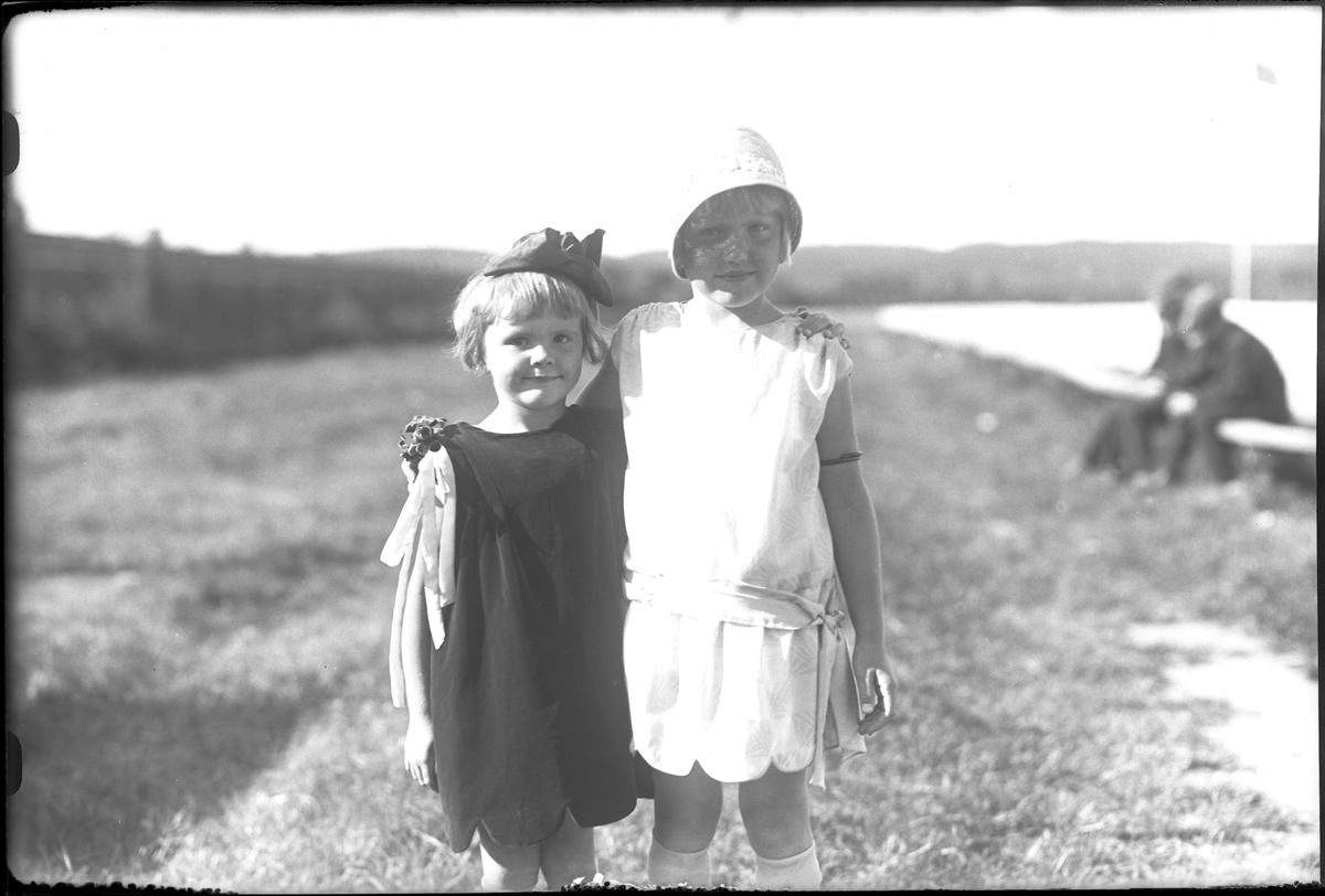 Två systrar håller om varandra. Den ena har svart klänning och hatt medan den andra har vitt. I fotografens egna anteckningar står det "Torsten Hallgrens flickor". Tolkat som Eima Viola Linnéa och Maj-Britt Maria Hallgren.
