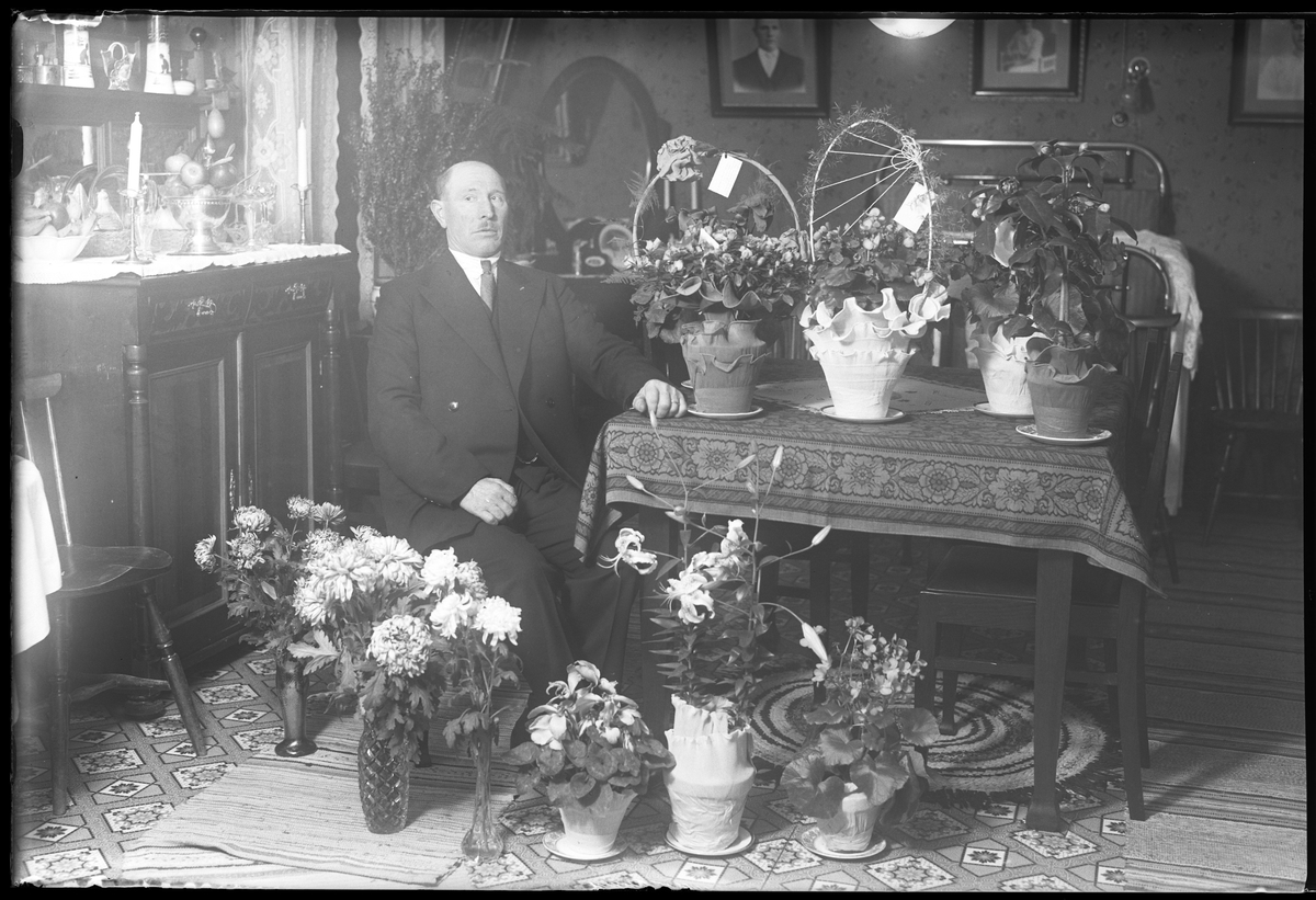 En man sitter vid ett bord i ett finrum, omgiven av blommor i samband med sin 50årsdag. I fotografens egna anteckningar står det "Gustaf Johanssons 50 år", tolkat som Anders Gustaf Johansson.
