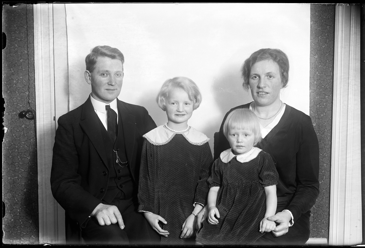 Familjeporträtt på familjen Dalén med mamma Tullie, pappa Carl samt barnen Ann-Marie och Margit. Familjen sitter framför en vit bakgrund och alla bär mörka kläder. I fotografens egna anteckningar står det "Carl Dahlén med familj".