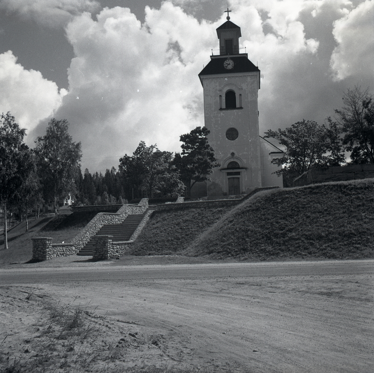 Ilsbo kyrka med en stentrappa och stenräcke i förgrunden.
