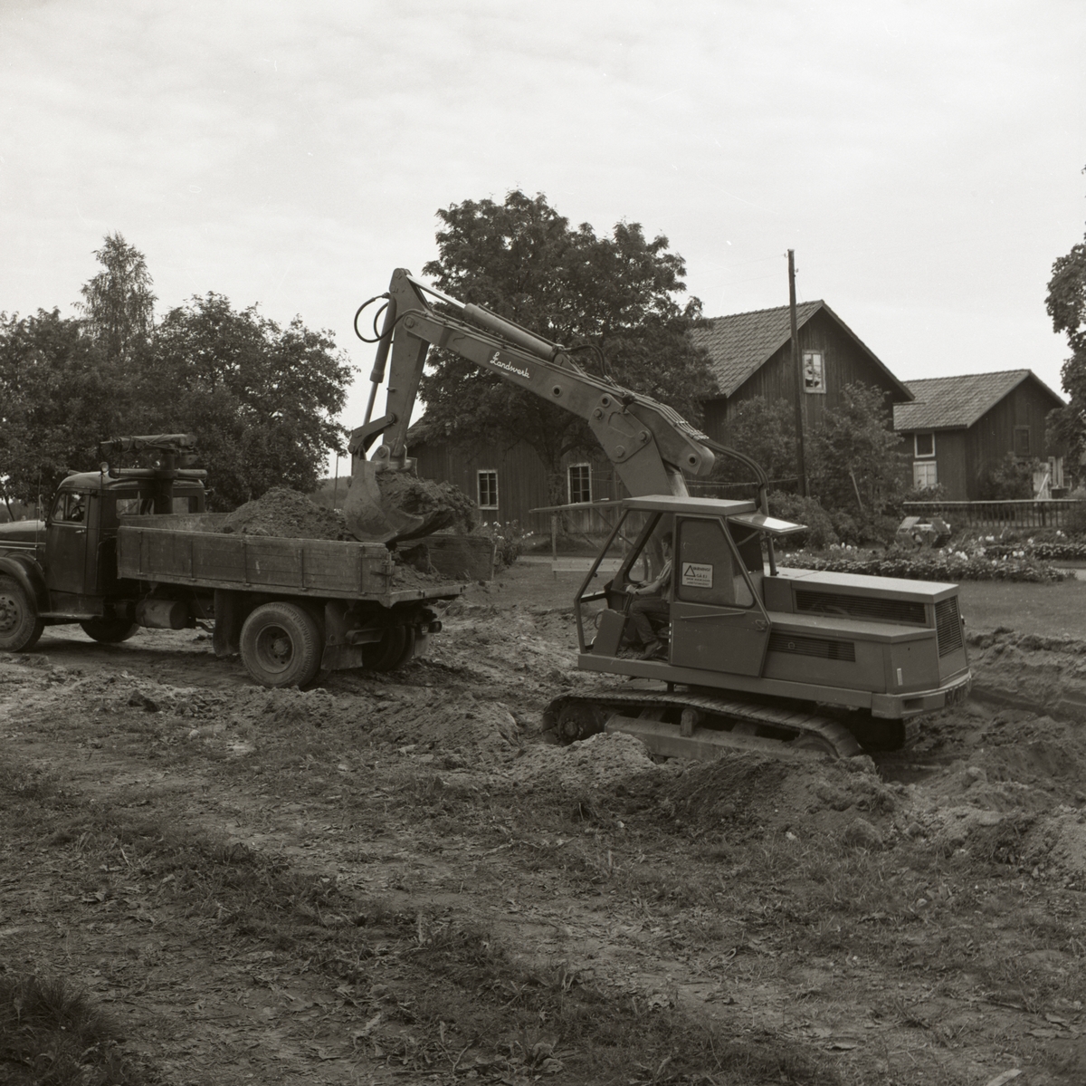En grävmaskin lastar jord på en lastbilsflak vid gården Sunnanåker, 1967.