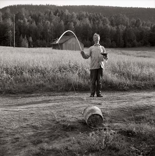 En person försöker dra till sig en hink genom att använda kroken på et metspö, 1968.
