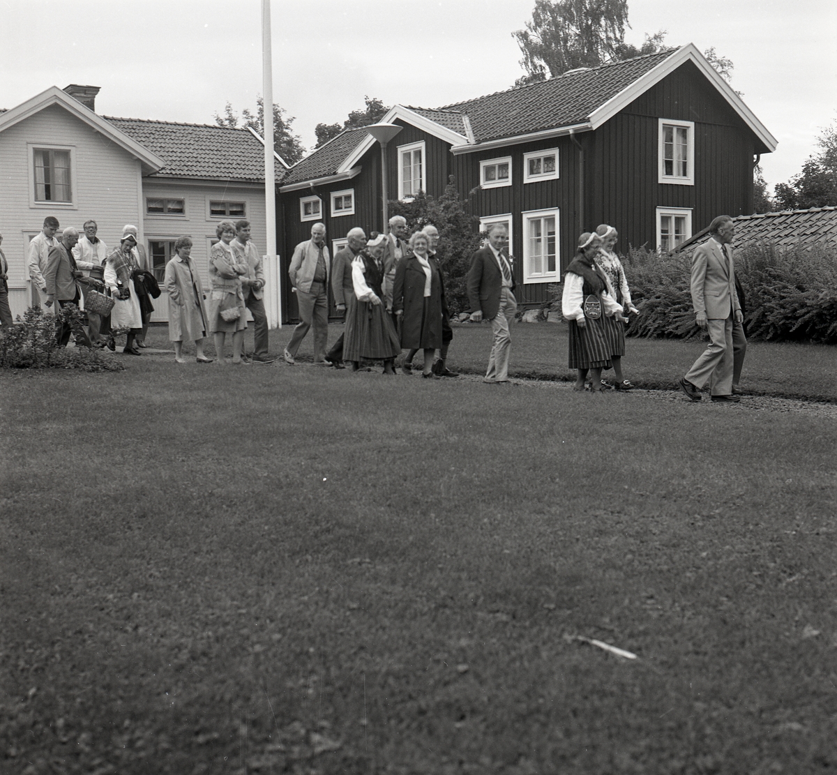 En grupp kvinnor och män går över en grusgång framför en gård i Njutånger den 7 september 1985.