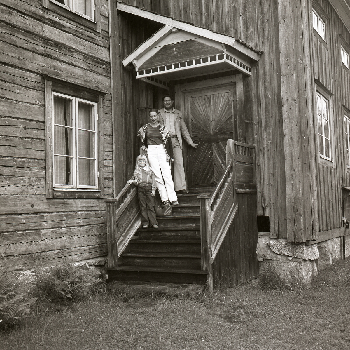 En man, en kvinna och ett barn står på en trappa utanför ett hus i Hembygdsbyn, 20 juli 1979.