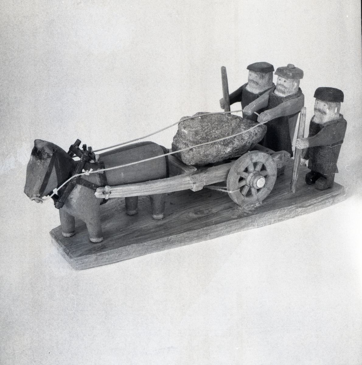 En modell föreställande tre figurer och en häst med vagn i trä.