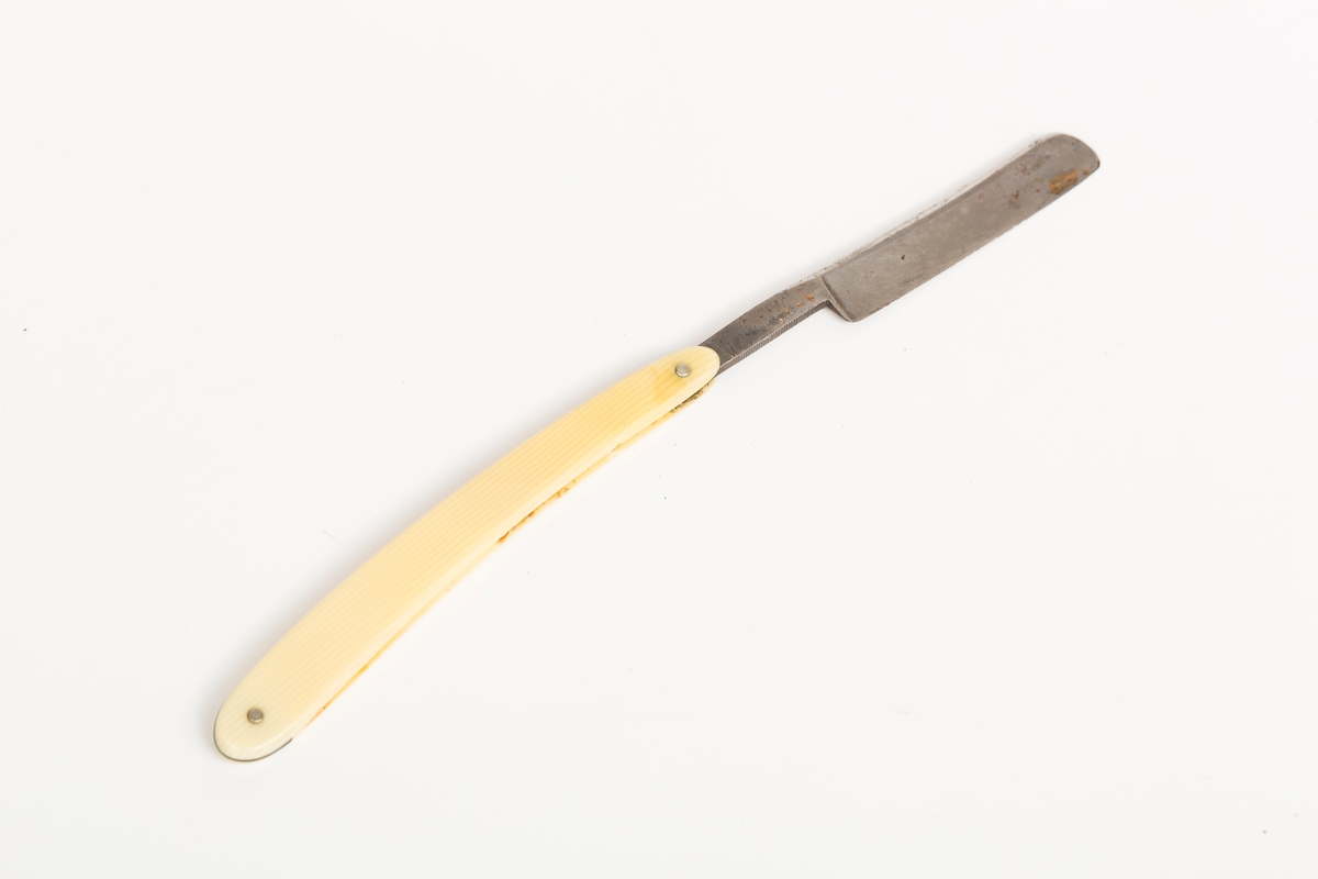 Barberkniv i stål med skaft i gulhvit plast.