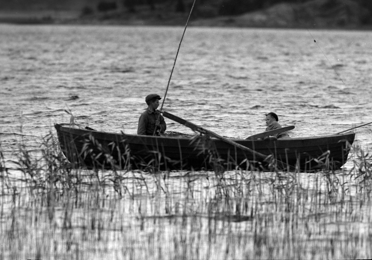 Två pojkar sitter i en roddbåt. Den ena håller i ett metspö. I fotografens anteckningar står det "35 films fr. semester på Halö".