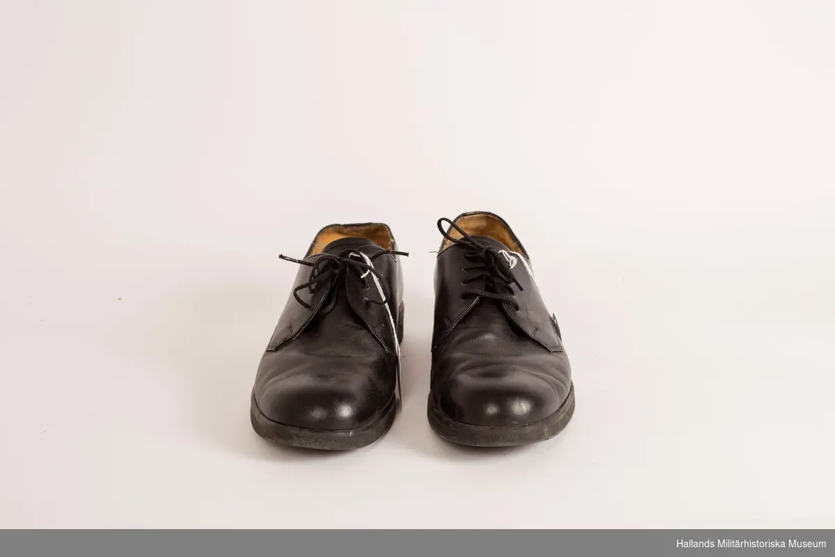 Ett par svarta lågskor, i läder med utanpåliggande raksömmar. Svarta gummisulor. Snörning på ovansidan av skorna med tunna svarta textilsnören. Hålprägling på plösen: 44 H. På innersulorna bär skorna kronstämpeln samt är märkta: 44 H, A & O. Skorna är märkta på insidan, höger kant med vit stämpel: 44 H833519 7 D.
