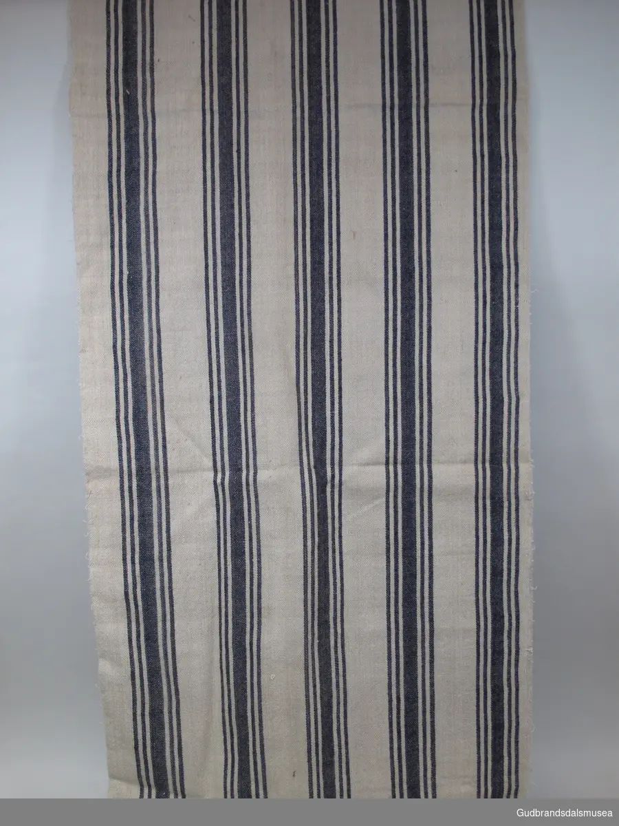 1 lengde vevd klede på ca. 370 cm lagt sammen og sydd i lengden, slik det utgjør halvdelen av et dynetrekk til underdyne, dvs. madrass. 1 av 3 kleder med likt stoff, veving og mønster med brede, vertikale striper i blått.