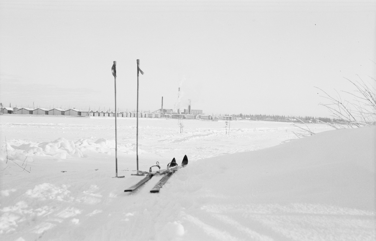 Ett par skidor med stavar är lämnade i snön vid Svenska frivilligkåren i Finland, F 19. I bakgrunden syns ett fält Kemi samhälle.