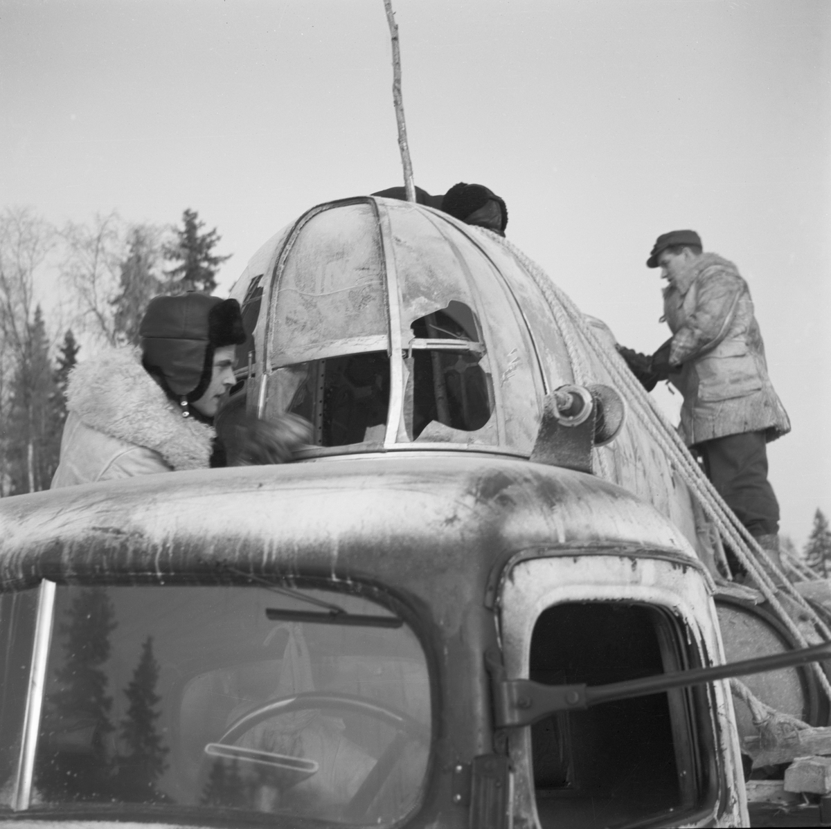 Transport av nedskjutet sovjetiskt flygplan DB-3 vid Svenska frivilligkåren i Finland, F 19. Säkring av flygplanet lastat på vagn efter lastbil. Tre militärer i arbete.