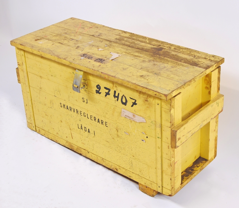 Skarvreglerare i två stycken gulmålade transportlådor av trä. Skarvreglerarens delar är också gula. På den ena lådan (:1) står det "SJ SKARVREGLERARE LÅDA 1" samt "SUO. ML.", vilket är förkortning för signalunderhållsområde Mellerud. Lådan är även märkt "27407". På den andra lådan (:22) står det "SJ SKARVREGLERARE LÅDA 2" samt "4". På låda 2 sitter även en adresslapp med godsavsändare SJ Huvudförråd, Bollnäs och mottagare "SJ Banområde Stationshuset Storvik".
Skarvregleraren består av en hydraulpump (handpump) (:24), ett handtag till pumpen (:25), sex stycken spännklotsar (:26-31), två stycken spännanordningar (:2-3), tio stycken shims (:6-15), sex stycken isolerskarvar (:4-5, :16-19), ett snörnystan (:20), fjorton stycken plastringar (:21) samt en tillhörande tratt för påfyllning av hydraulolja (:23). I lådan fanns även en följesedel och en instruktion från november 1965 "SJ CENTRALFÖRVATNING BANAVDELNINGEN Rationaliseringskontoret". Instruktionen, som består av ett A4 ark med text och bild på båda sidor, är helt dränkt i hydraulolja. 

Text på instruktionen "Skarvregleraren är avsedd för användning vid signalunderhållsområdenas arbeten med isolerskarvar. 
Den består av 8 spännklotsar, (4 st för SJ50 och 4 st för SJ34, SJ41 och SJ43) 2 st hydrauliskt arbetande spännanordningar, hydraulpump samt 8 st mellanlägg. 
Hydraulpump: Dowty HP 5, arbetstryck 150 kg/cm2
Hydraulolja: H O L 25 (fdnr 10 24 732)

Anvisning för uppmontering
Skruva loss skarvjärnen och montera spännklotsarna
Placera spännanordningarna på plats och koppla ihop hydraulslangarna
Koppla hydraulslangen till hydraulpumpen.
Stäng avlastningsventilen.

Anvisning för nedmontering
1.Öppna avlastningsventilen
2.2. Återför hydraulcylindrarnas kolvstänger till utgångsläget
3.Koppla isär hydraulslangarna
4.Lyft loss spännanordningarna
5.Skruva loss spännklotsarna

VIKTIGT! Skydda slagändarna mot grus och andra föroreningar."

Måtten i blanketten gäller låda 1. Låda 2, lxbxh: 760x430x345 mm.

Se bilaga till samlingar.

Modell/Fabrikat/typ: SKARVREGLERARE TYP SRI