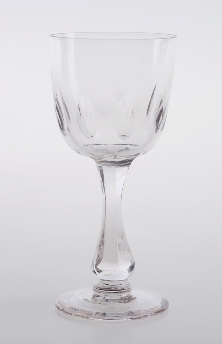 Et hetvinsglass laget av klart glass. Det er en langstrakt klokkeformet cupa med olivenslipninger i nedre del av klokken. Stetten er balusterformet. Stetten er slipt slik at den er seks-kantet.
