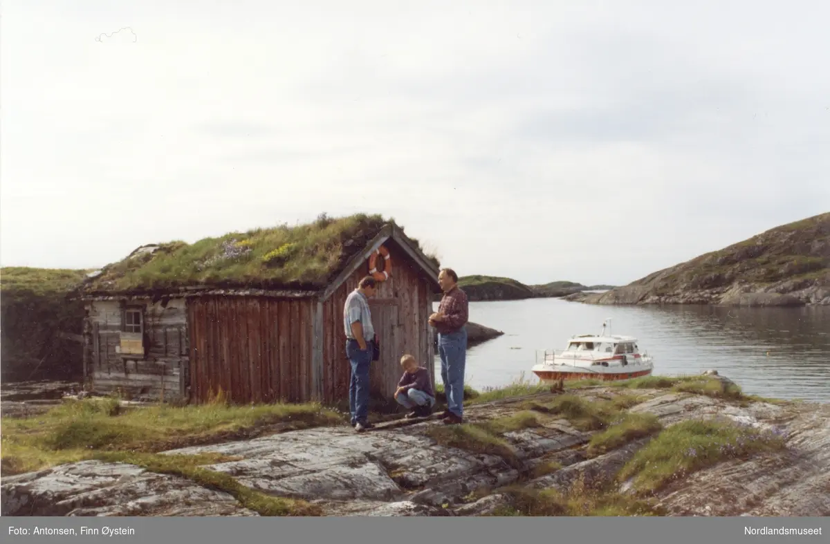 Gildeskål. Fleina. Fleinholman. Tre personer foran en av buene i Fleinholman. Mannen til høyre er Finn Antonsen. Båt fortøyd i bakgrunnen.