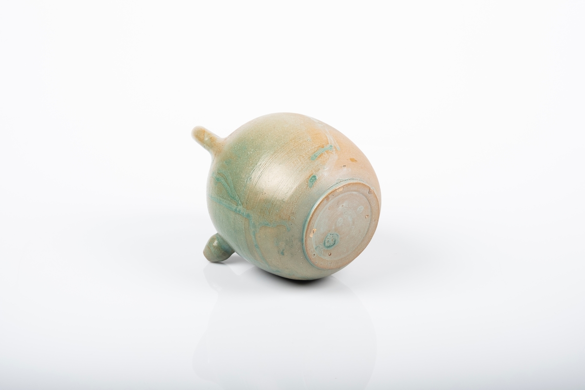 Keramikkanne trolig brukt som tekanne eller vannkanne. Den mangler/har ikke lokk. Den er dreid og har rund form med hank over åpningen. Liten høyt plassert tut. Den er delvis glasert med grønn glasur.