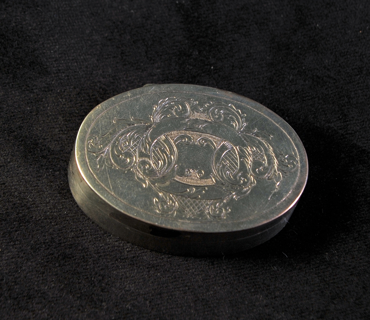Oval dosa av silver. Graverad dekor i nyrokoko på locket. I botten ingraverade initialer: "J.C.J.S.". Invändigt förgylld med spegel i locket. Stämplad i insida i botten.